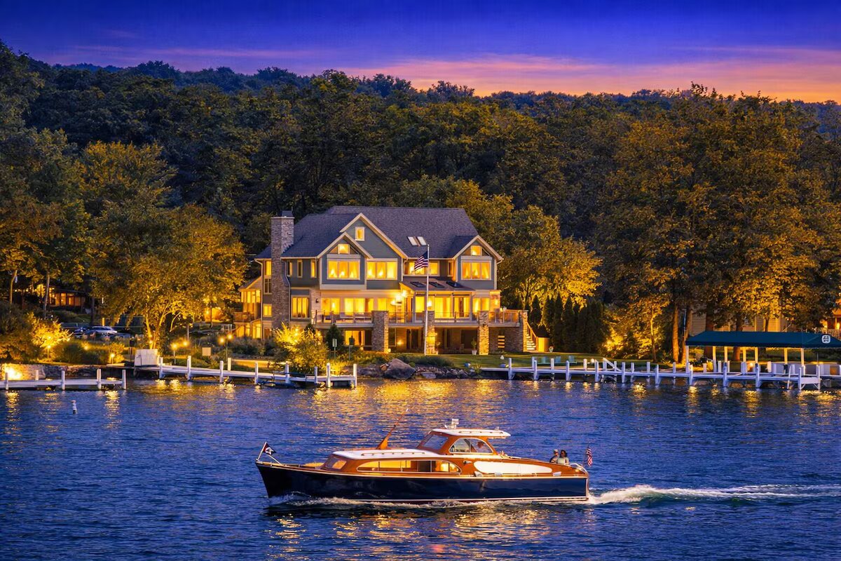 Lakefront Lake Geneva mansion lit up at twilight with a wooden boat passing